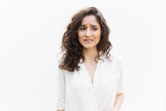 Upset woman realizing mistake, feeling guilty, looking away. Wavy haired young woman in casual shirt standing isolated over white background. Stress or error concept