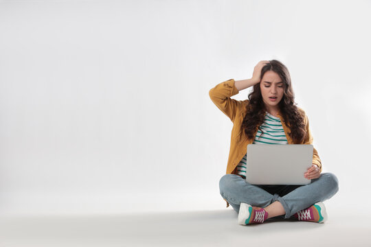 Shocked young woman sitting with laptop on white background