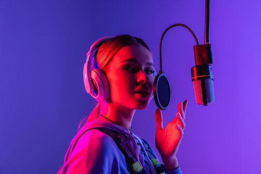 young singer in wireless headphones singing song in microphone on purple