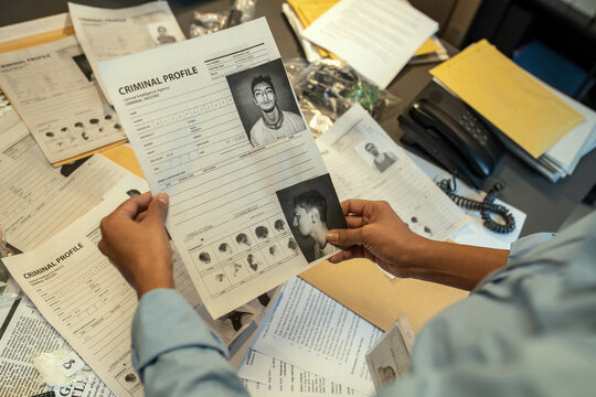 Hands of young female FBI agent holding document with personal data of criminal during investigation assignment in office