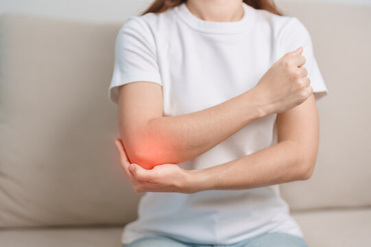 Woman having elbow ache during sitting on couch at home, muscle pain due to lateral epicondylitis or tennis elbow. injury, Health and medical concept