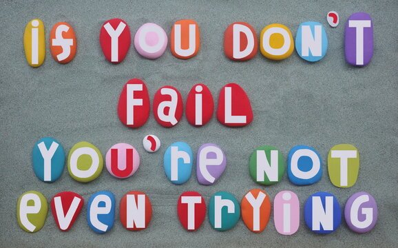 If you don't fail you are not even trying, motivational life quote composed with hand painted multi colored stone letters over green sand