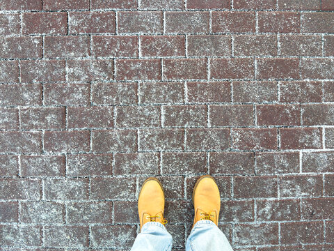 Icy sidewalk with anti-icing reagents improves traction. Winter boots stands on road with de-icing chemicals, reducing accidents by slippery conditions. Technical salt for safety in freezing weather.