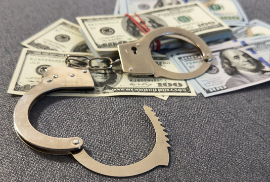 Financial crime, fraud, money laundering, corruption, or law enforcement : Bundles of US dollar 100 bills in a small case, alongside a pair of handcuffs placed over the US dollar currency.