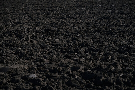 Dark soil lies freshly turned in a rural landscape as dusk settles. The rich earth reveals small stones and texture, indicating readiness for planting. Freshly plowed field. Close up