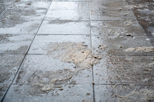 Deicing chemicals on pavement in winter. Salt grains on icy sidewalk, paving slab with rock salt in cold season. Slippery road sprinkled with technical salt and calcium. Prevent slipping concept