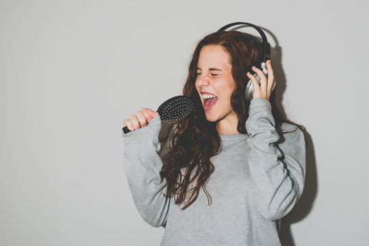 Young ginger girl singing and listening to music in wireless headphones