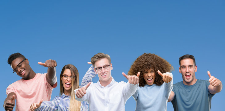 Composition of group of friends over blue blackground approving doing positive gesture with hand, thumbs up smiling and happy for success. Looking at the camera, winner gesture.