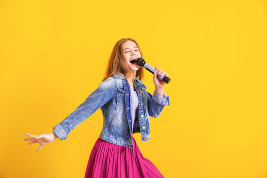 Teenage girl with microphone singing against color background