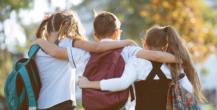 school friends a boy and two girls with school backpacks on their backs walk after class