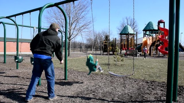 Father Pushing Son on Swings at the Park.