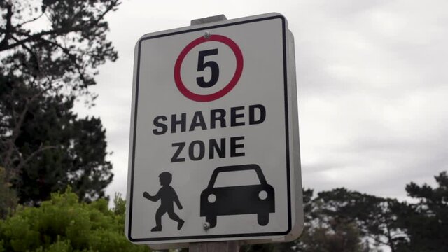 Five-kilometer miles speed limit shared zone sign with an illustration of pedestrian and car with trees in the background.