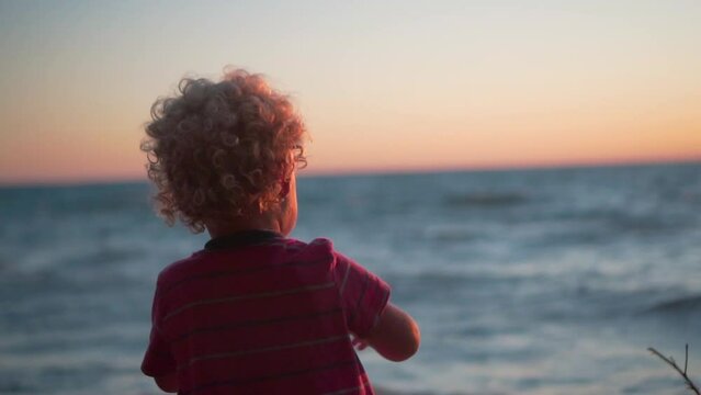 Slow Motion Shot of Young Boy Throwing Rocks into the Sea at Sunset