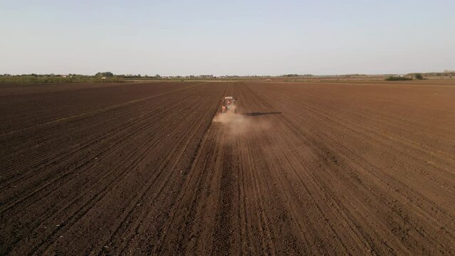 Aerial rear view of tractor harrowing a field at sunset.