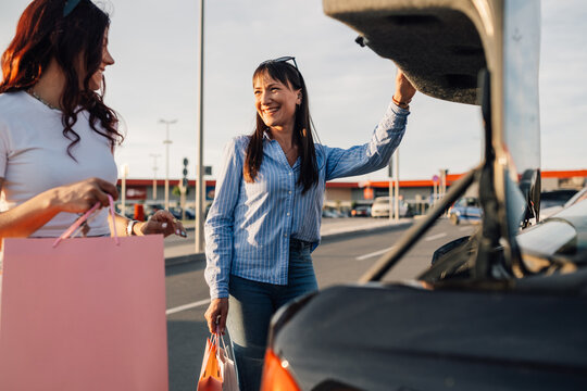 Trendy girls putting shopping bags into a trunk after shopping spree.