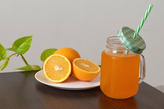 A picture of oranges cut into two pieces and a mason jar full of orange juice kept alongside the plate on a hot sunny day.