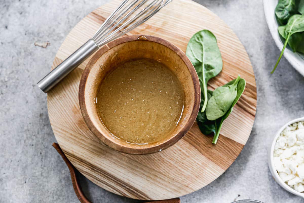 A homemade salad dressing in a wooden bowl made of apple cider vinegar, olive oil, dijon mustard, honey, and salt and pepper.