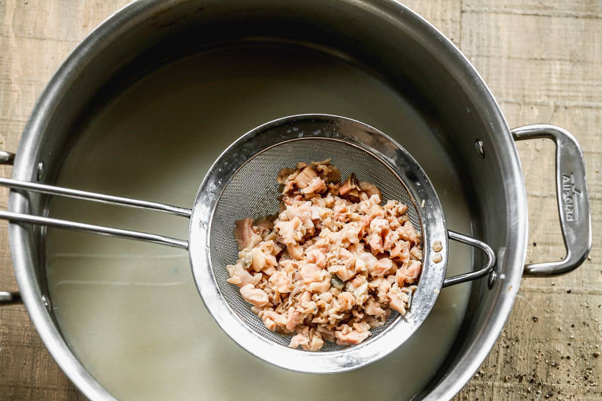 Canned clams in a metal strainer above a large pot, drained.