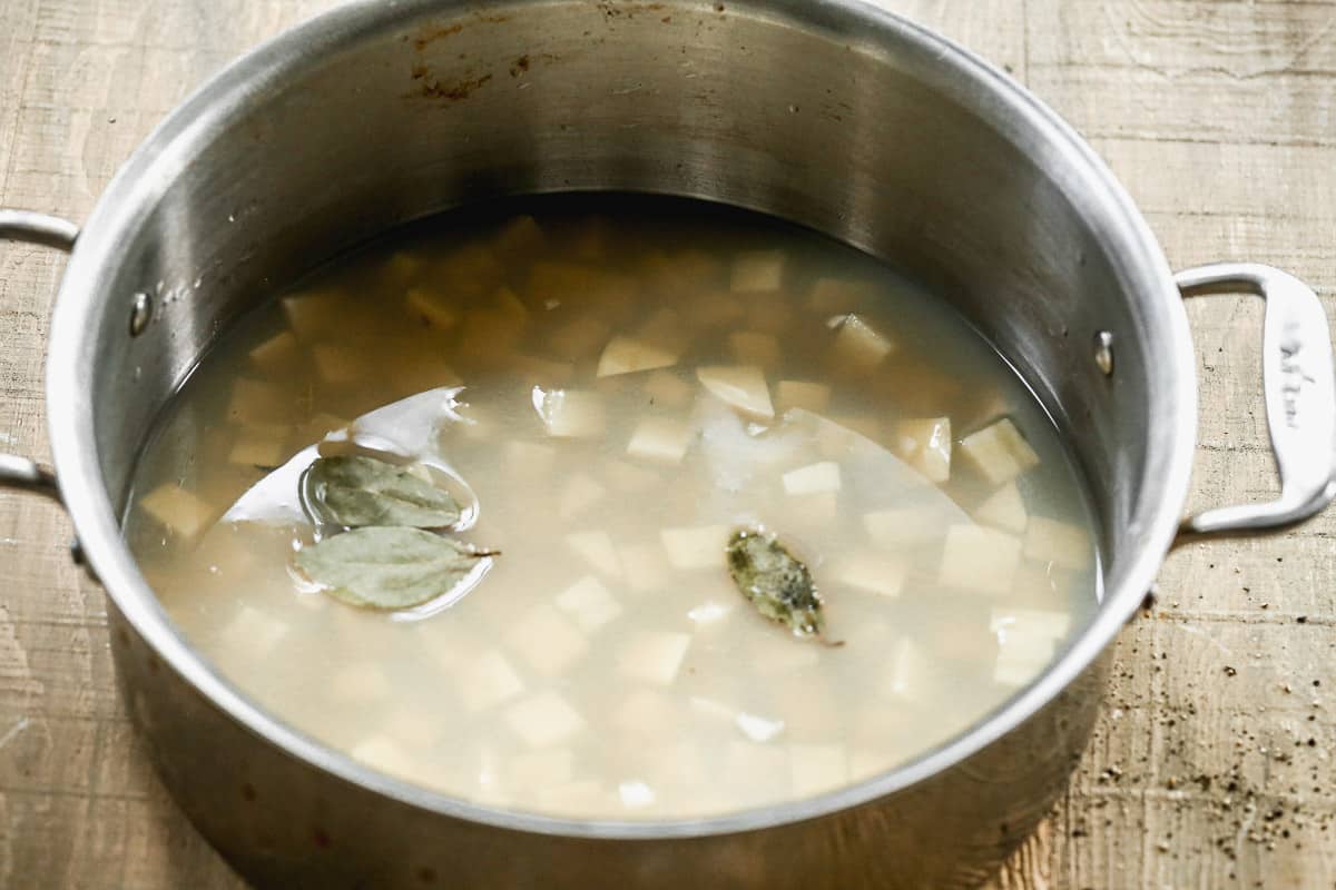 A pot with chopped potatoes and water, with a few bay leaves floating on top.