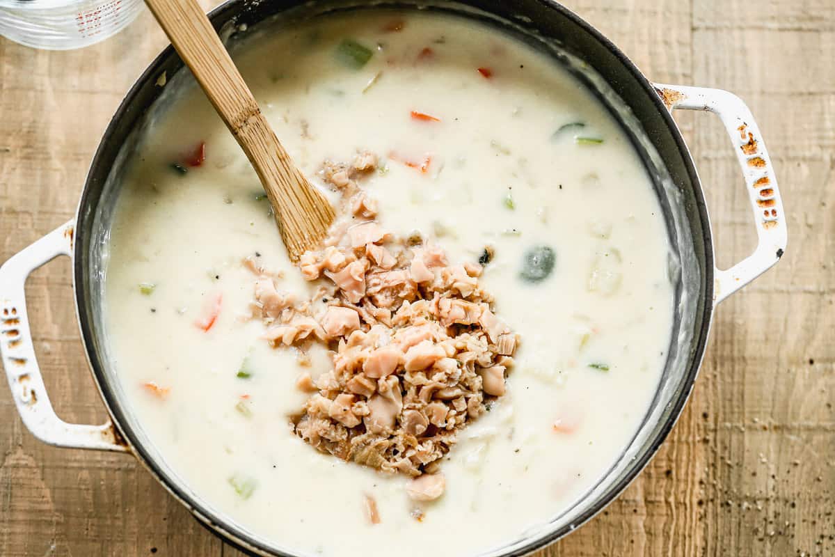 Chopped clams being stirred into a creamy broth for easy homemade Clam Chowder.