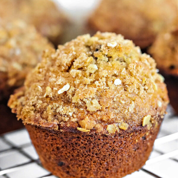 A close-up of an oatmeal raisin muffin with a crumbly oat topping resting on a cooling rack.