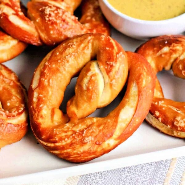 A plate of golden-brown pretzels, reminiscent of soft Auntie Anne’s delights, served with a small bowl of mustard dipping sauce.