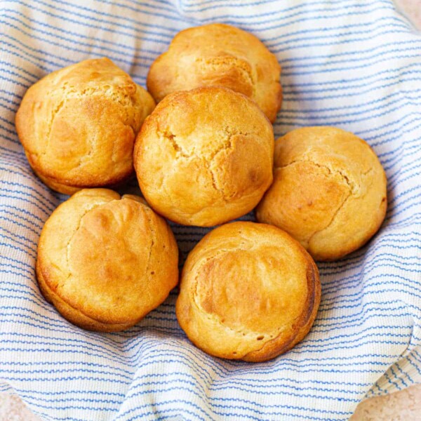 Golden brown mayonnaise biscuits rest in a striped cloth-lined basket on a light textured surface.