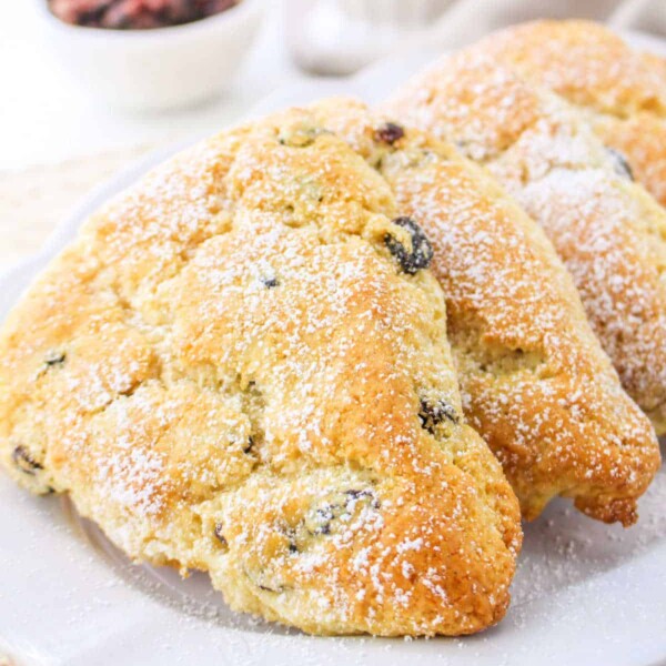 Three golden, triangular Bisquick scones dusted with powdered sugar rest elegantly on a white plate.