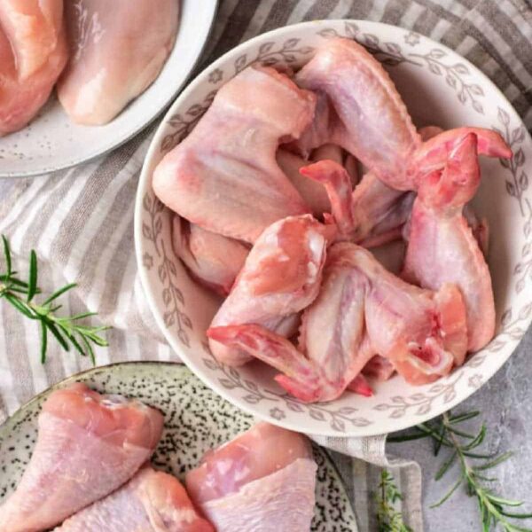 Bowls of raw chicken wings, drumsticks, and breasts sit on a striped cloth, each garnished with sprigs of rosemary, inviting you to consider how many ounces of meat in a pound youll need for your next delicious meal.