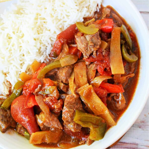 Plate of slow cooker pepper steak with bell peppers and rice, served with chopsticks.