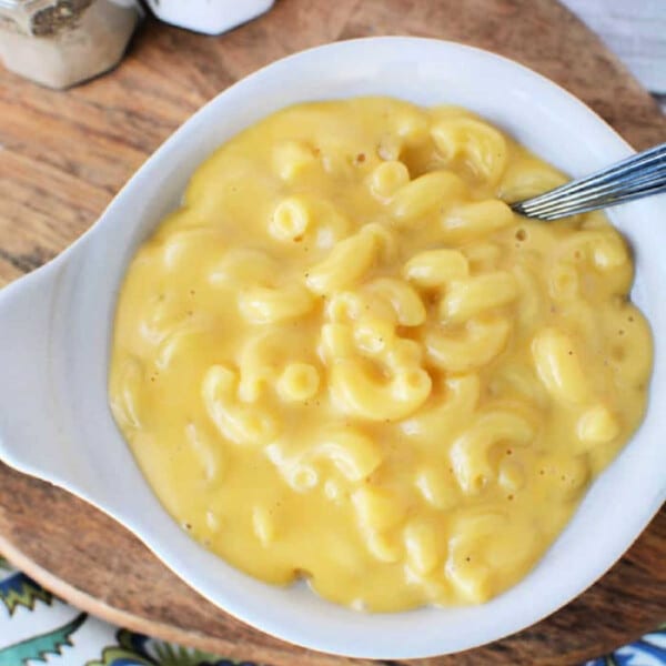 A bowl of creamy macaroni and cheese, made effortlessly in the microwave, sits with a fork on a wooden board beside salt and pepper shakers.