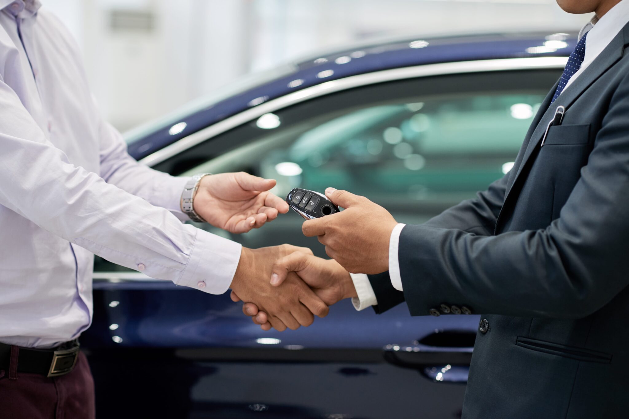 Independent Car Dealer handing car keys to customer while shaking his hand.