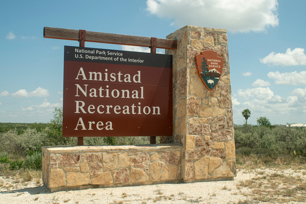 a sign with a stone base that reads Amistad National recreation area on a sunny day