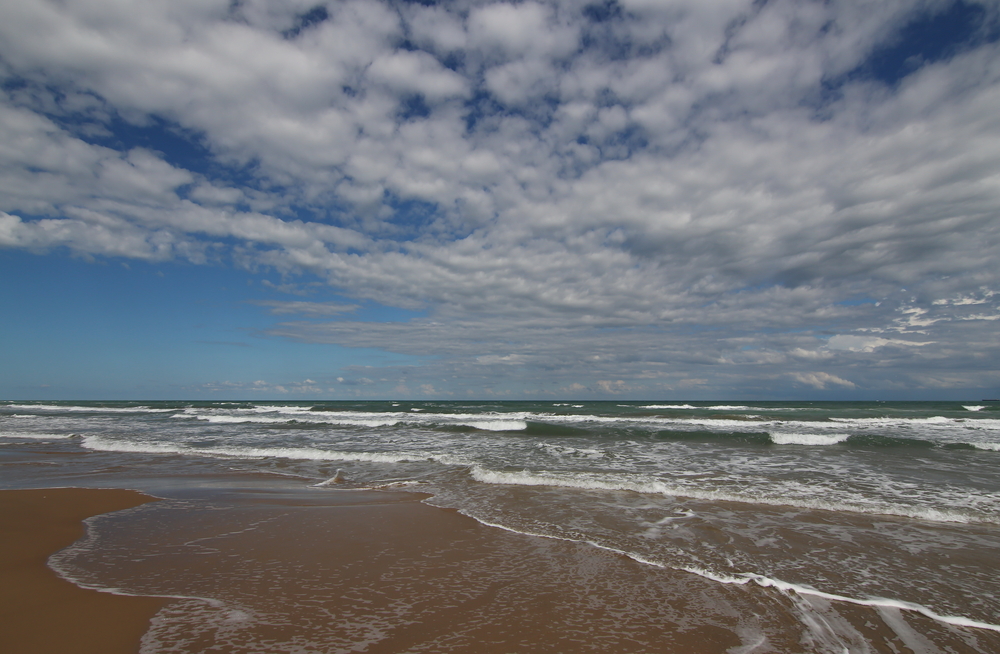 waves crashing onto the shoreline of a beach on a sunny day