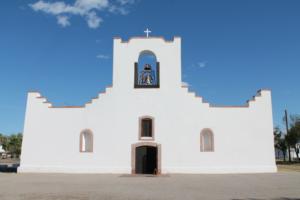 a white geometric shaped building with a bell in the top center on a sunny day