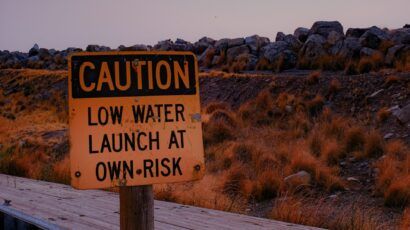 Sign reading "Caution Low Water Launch At Own Risk" at Great Salt Lake marina during a drought in front of naturally-colored grasses that look like fire.