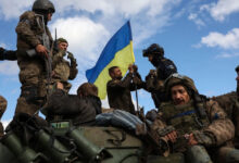 Ukrainian soldiers adjust a national flag atop a personnel armored carrier on a road near Lyman in the Donetsk region on Oct. 4, amid the Russian invasion of Ukraine