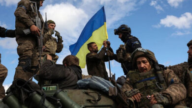 Ukrainian soldiers adjust a national flag atop a personnel armored carrier on a road near Lyman in the Donetsk region on Oct. 4, amid the Russian invasion of Ukraine