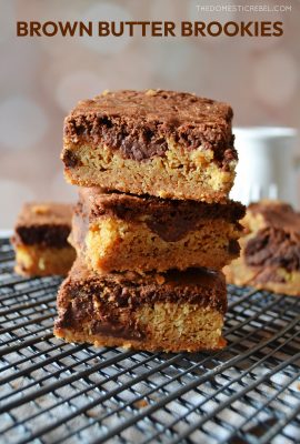 a trio stack of brown butter brookies sitting on a black baking cooling rack against a light colored background. a jar of milk sits in the background behind the brookies.