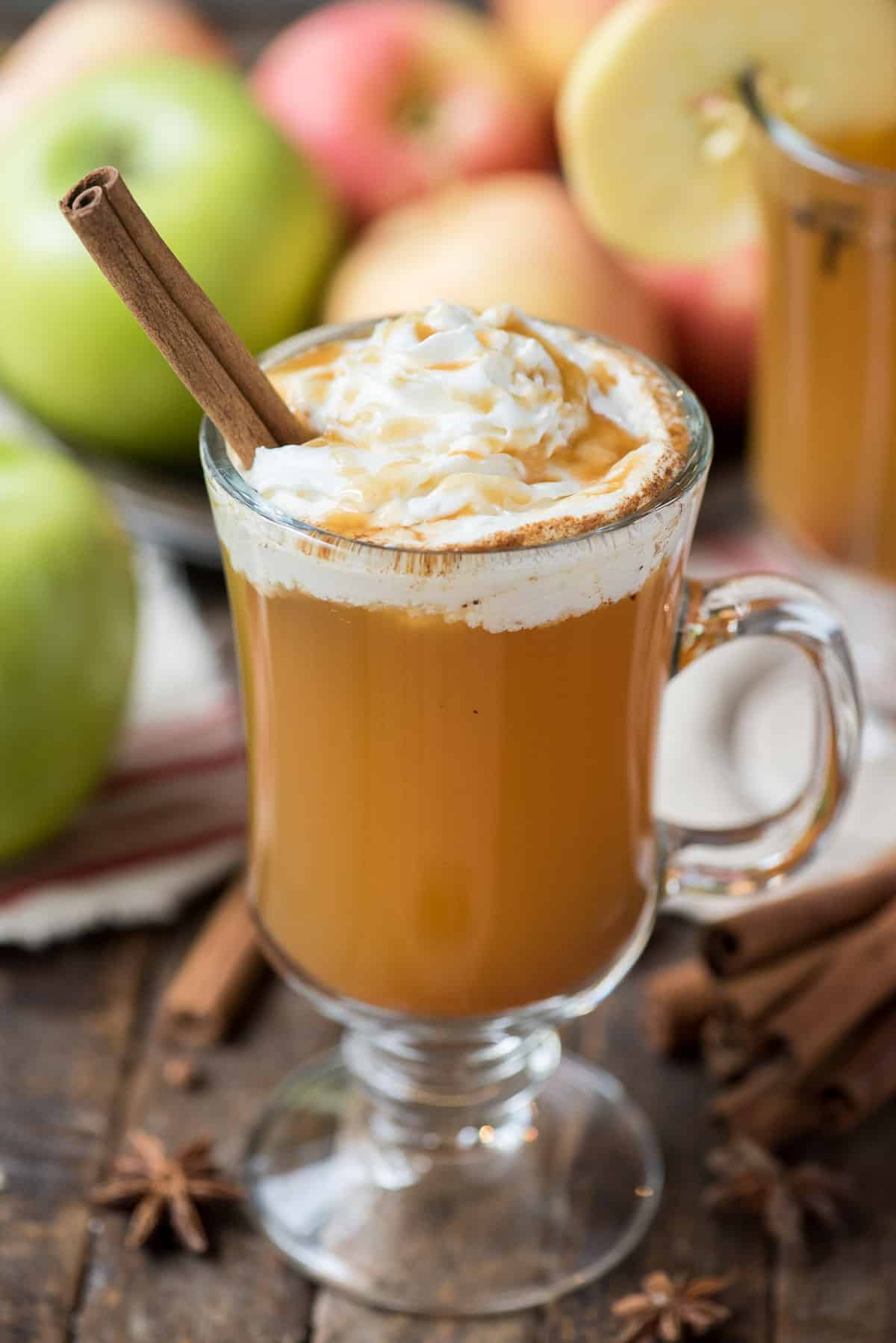 hot apple cider in clear glass with whipped cream and a cinnamon stick