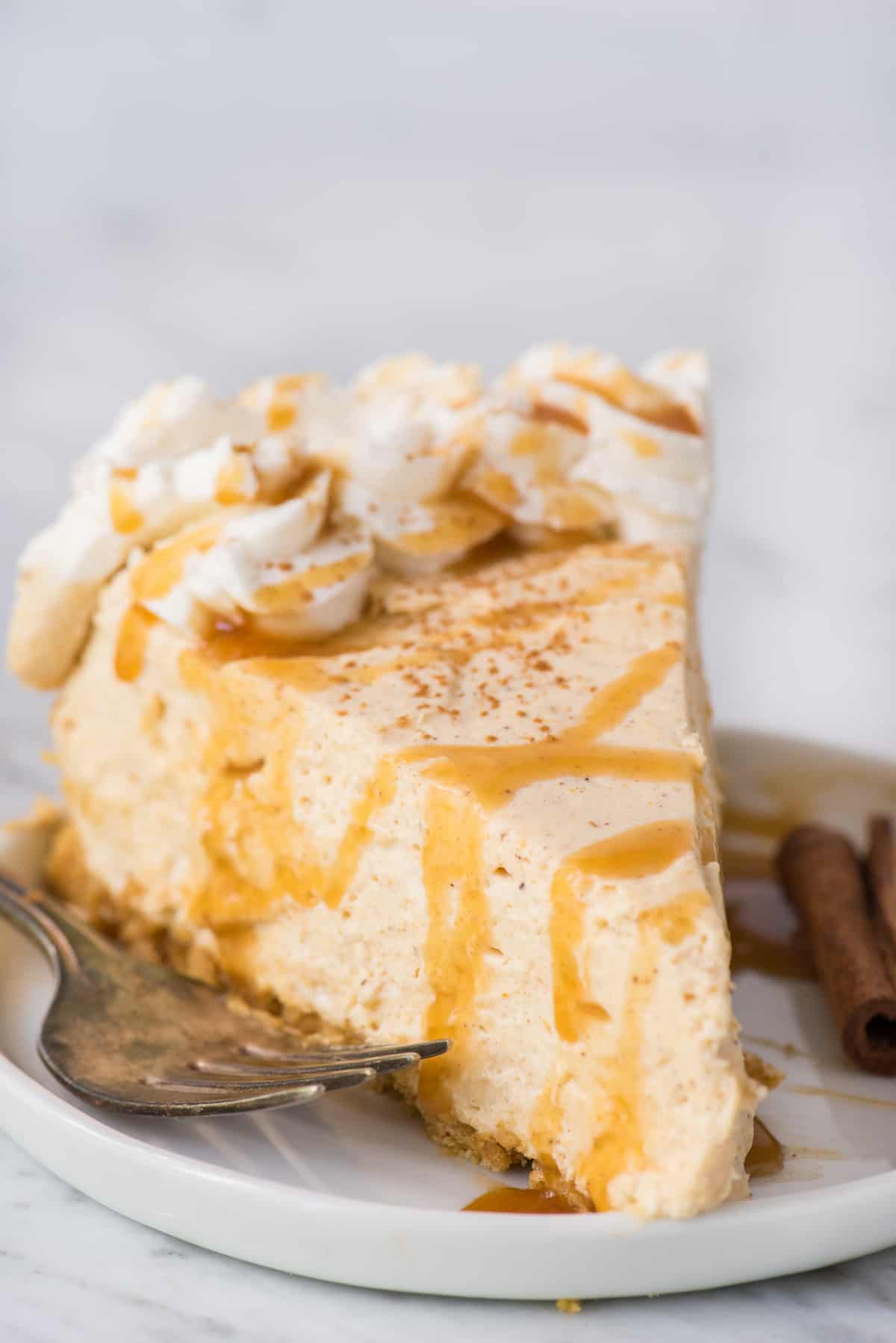 slice of no bake pumpkin cheesecake with caramel drizzle on top on white plate on white background