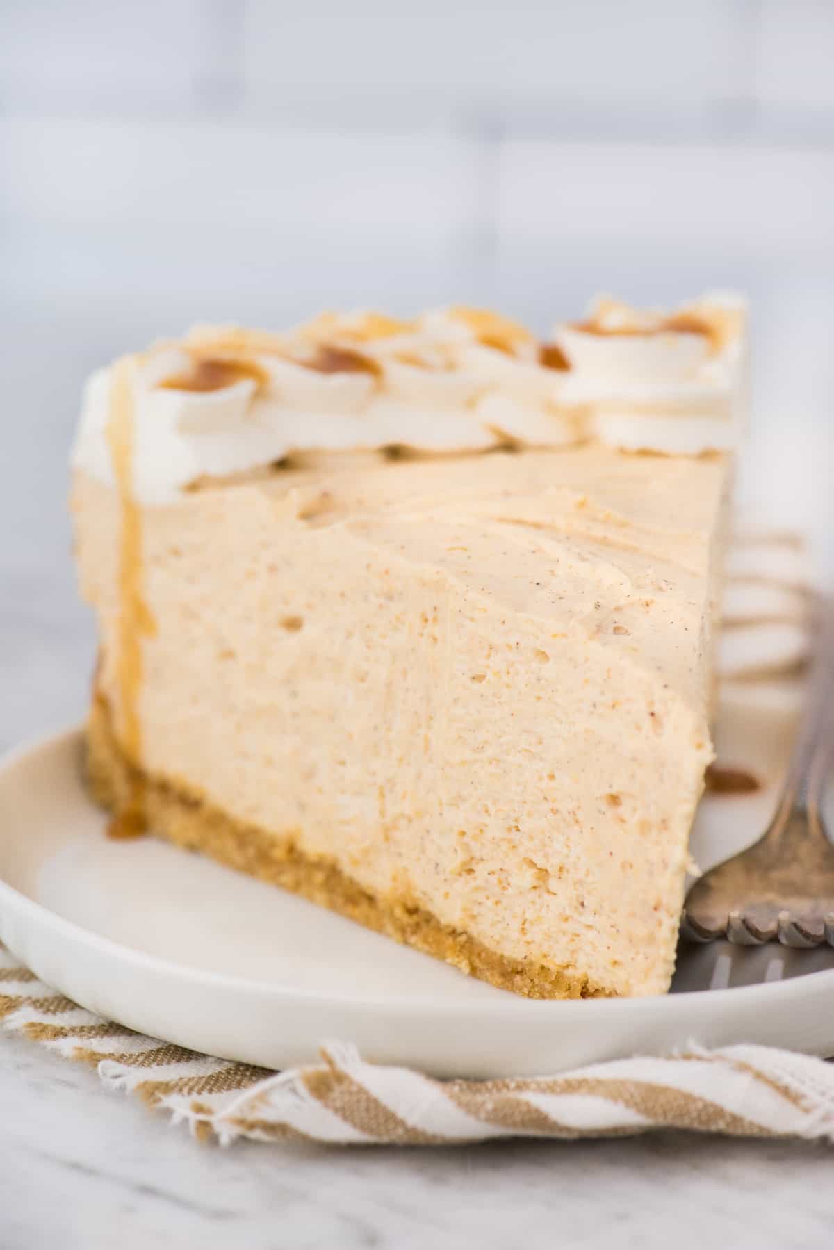 a slice of no bake pumpkin cheesecake on white plate with striped linen underneath the plate with white background