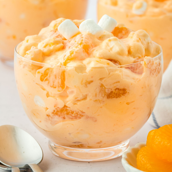 orange fluff salad in a bowl surrounded by mandarin oranges and a spoon