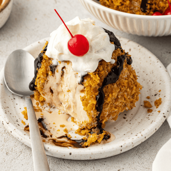 fried ice cream on a white plate with a spoon, topped with a cherry and whipped cream