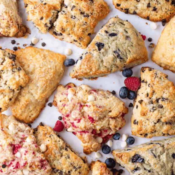 an assortment of scone flavors with fresh blueberries, raspberries and mini regular and white chocolate chips scattered around