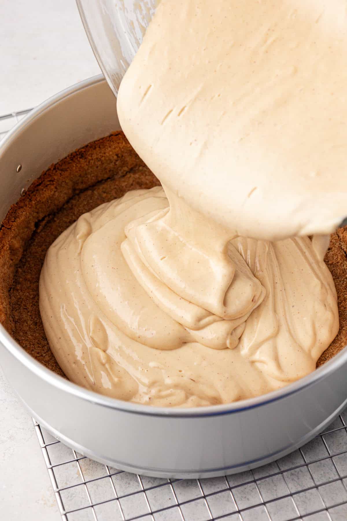 cheesecake batter being poured into a springform pan with graham cracker crust in it