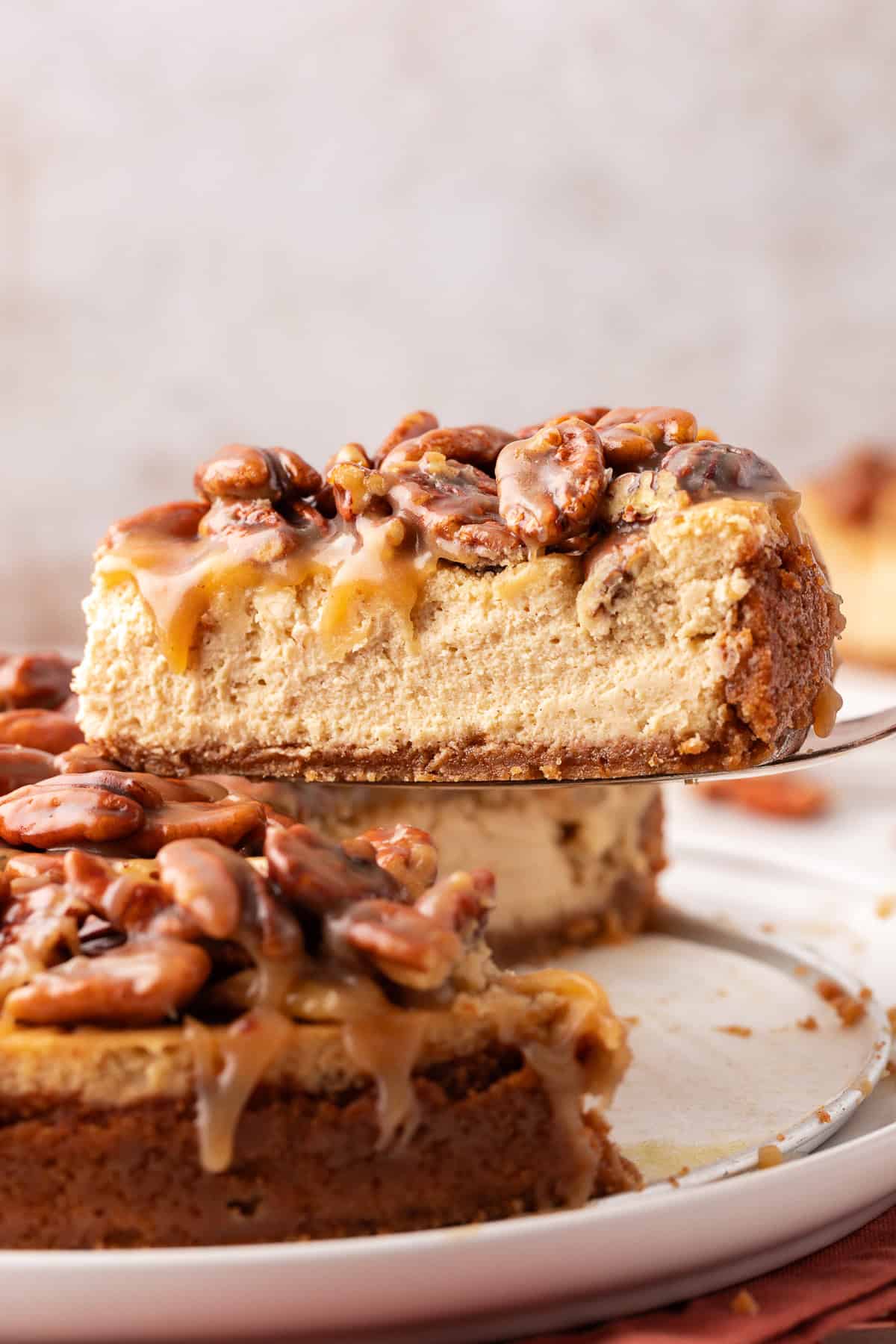 side view of a slice of pecan pie cheesecake lifted above the rest of the cheesecake with a serving spatula