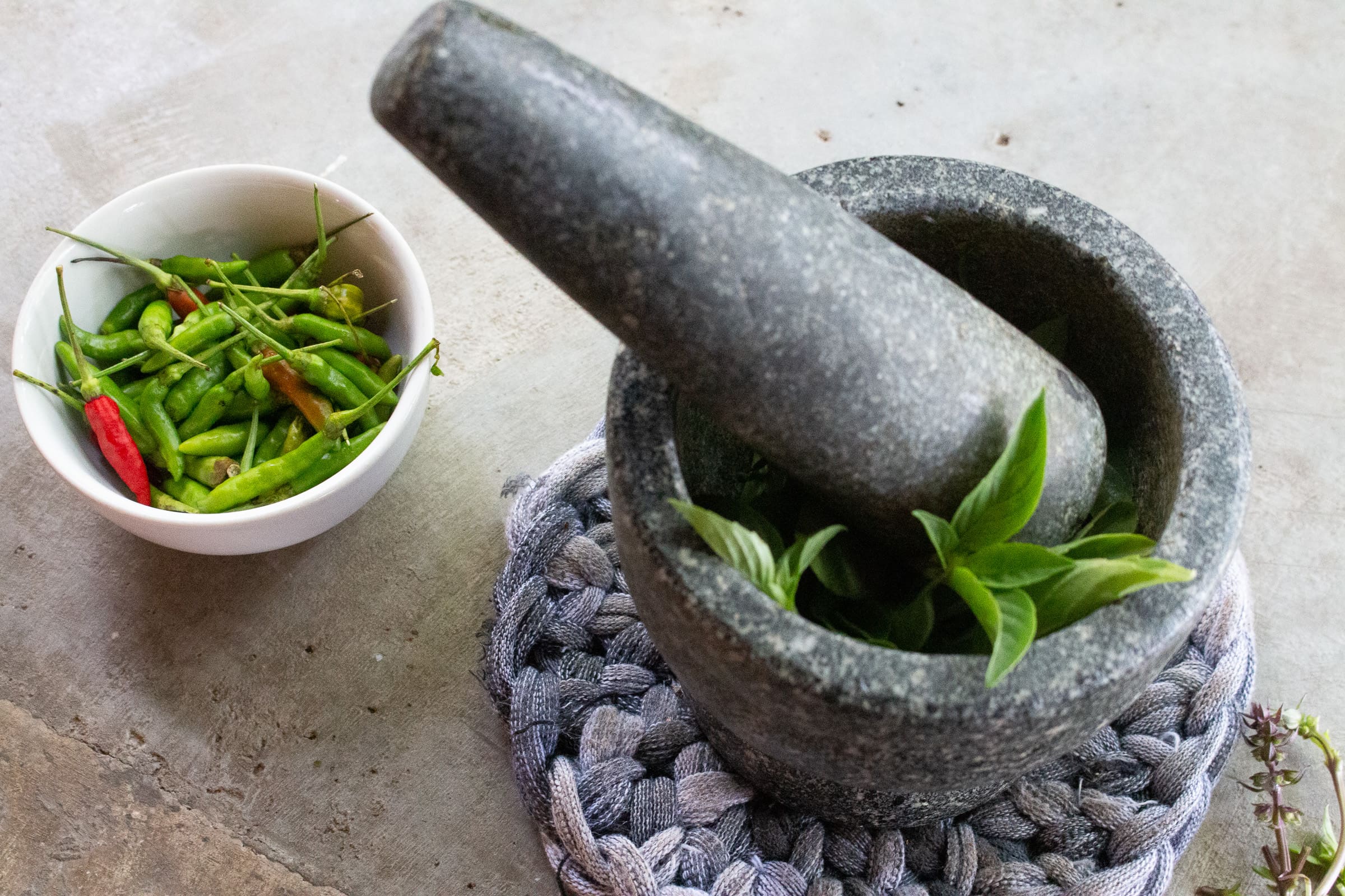 Mortar with herbs for curry paste and bowl with chilli peppers