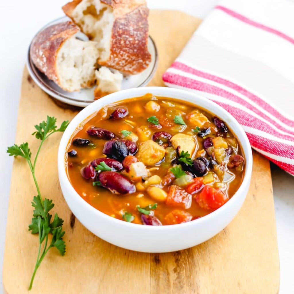 A bowl of three bean chicken soup on a wooden board.