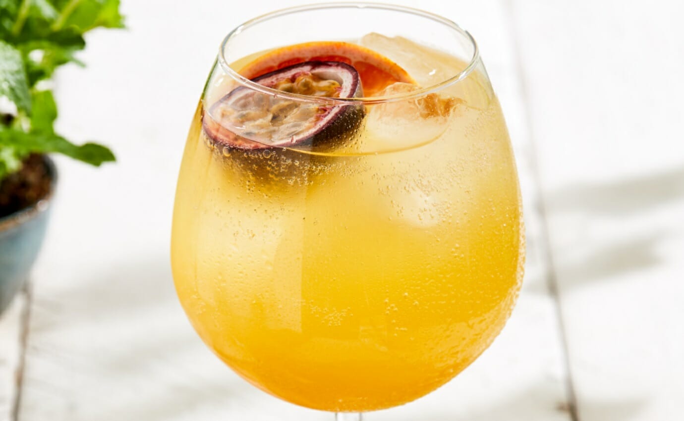 An iced called passionfruit spritz made in a large wine glass.